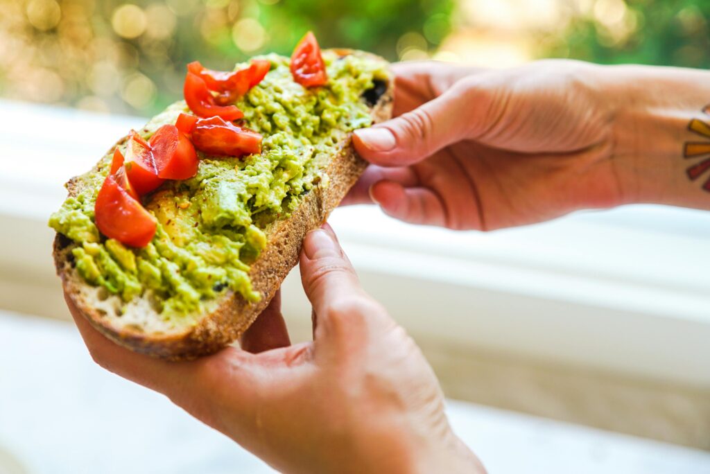 Close-up of avocado toast topped with cherry tomatoes being held by tattooed hands.